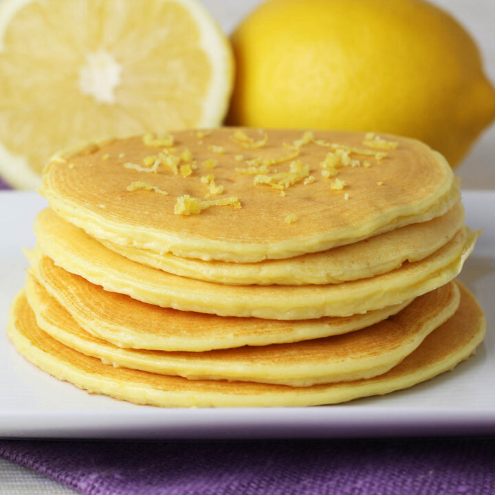 stack of lemon ricotta pancakes on a white plate with lemons in the background
